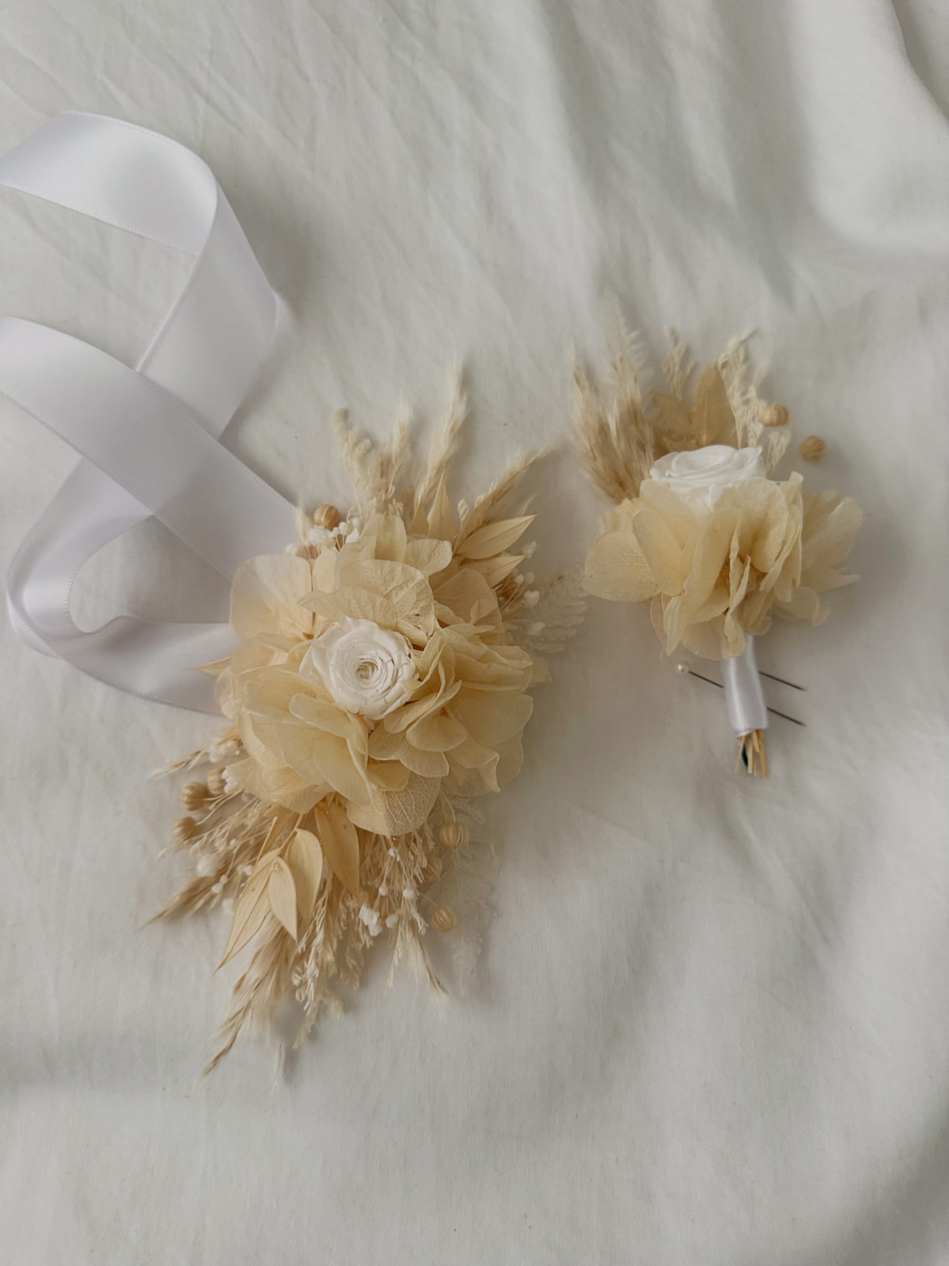 Two beige floral corsages with white ribbons on a light fabric background